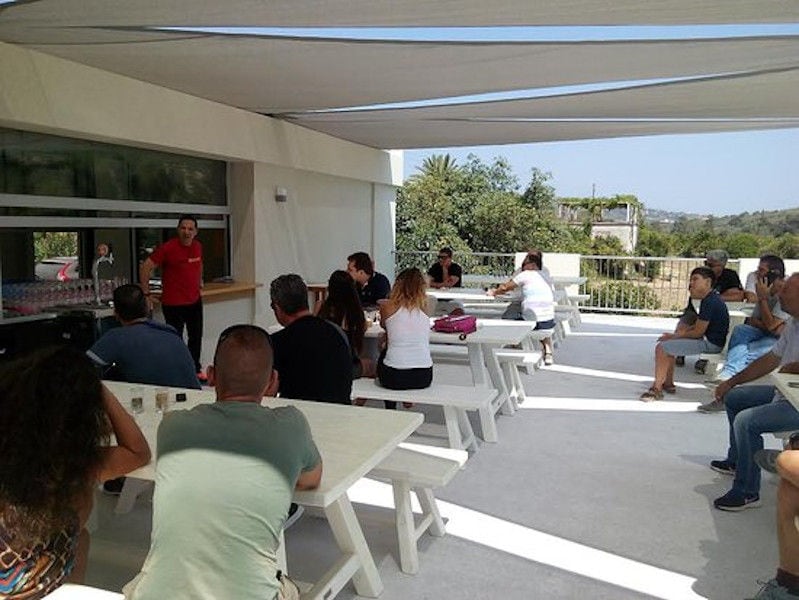 tourists sitting around the tables and listen the guide at Cretan Brewery facilities